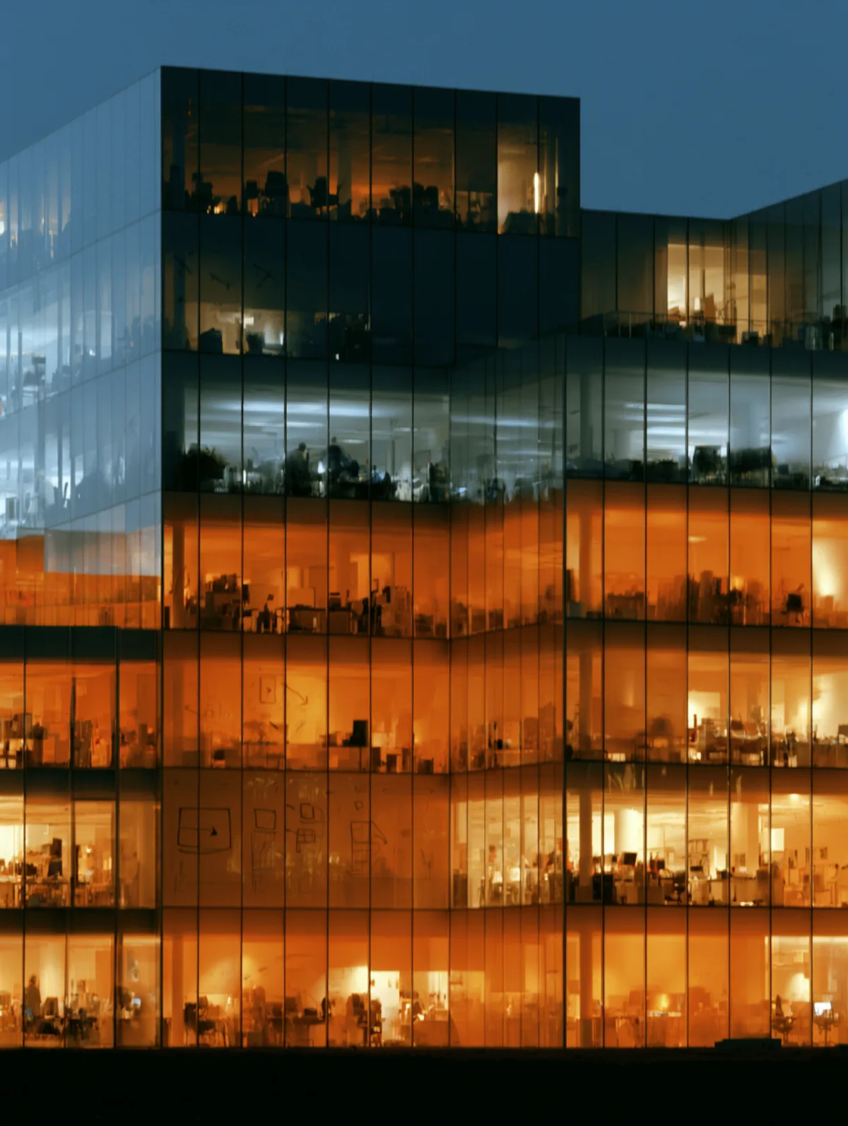A glass-fronted office block after dark, some floors lit warm and some cool